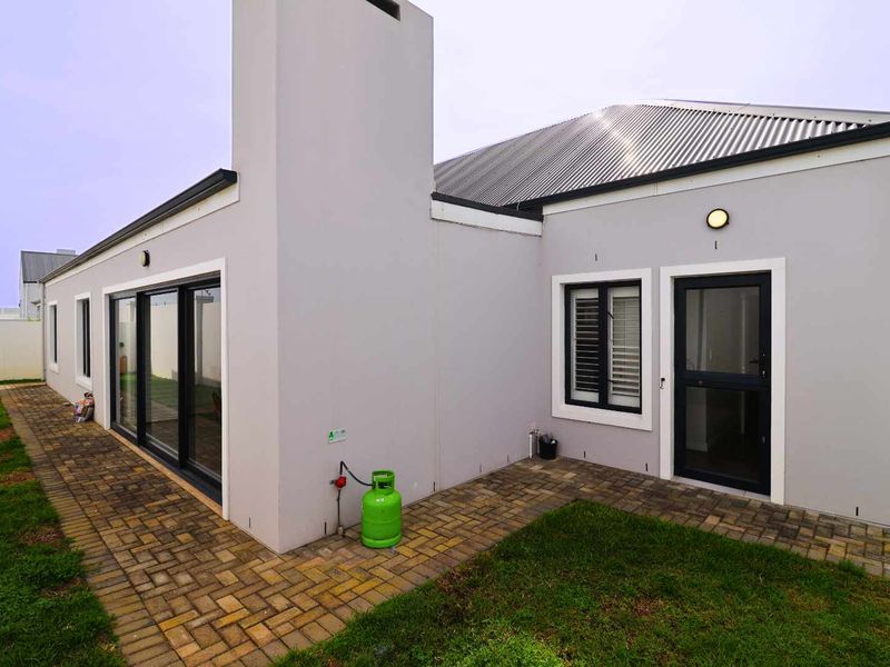 Rear view of the property featuring a paved walkway, corrugated metal roof, external chimney, and modern sliding glass doors leading to the garden.