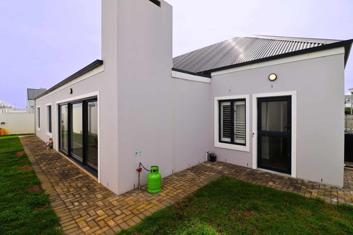 Rear view of the property featuring a paved walkway, corrugated metal roof, external chimney, and modern sliding glass doors leading to the garden.