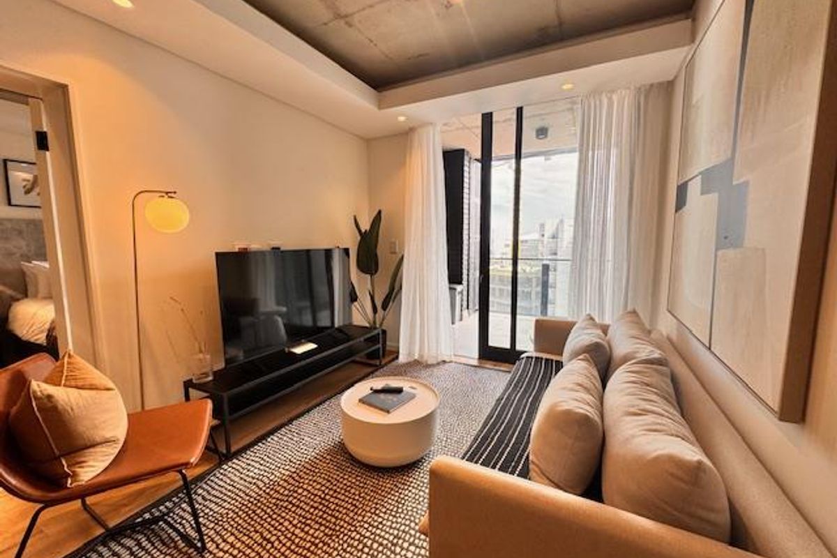 Modern living room featuring an exposed concrete ceiling, recessed lighting, and direct access to a private balcony through floor-to-ceiling glass doors.