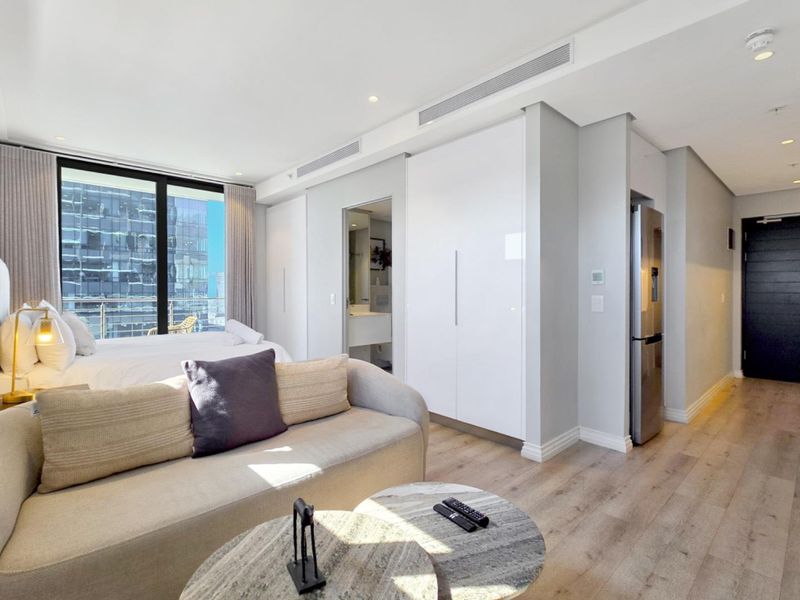 Modern open-plan studio apartment featuring timber flooring, built-in storage, ducted air conditioning, and access to a private balcony.