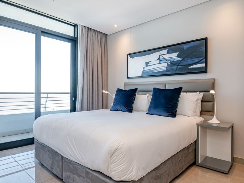 Modern bedroom featuring tiled flooring, an upholstered headboard, and a large sliding glass door providing access to a private balcony.
