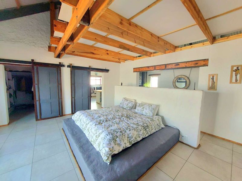 Spacious bedroom featuring exposed timber ceiling beams, tiled flooring, and a central half-height partition wall with sliding barn-style doors leading to adjacent areas.