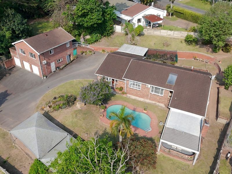 Aerial view of a residential property featuring a main house with a tiled roof, a swimming pool, a detached garage, and a paved driveway.