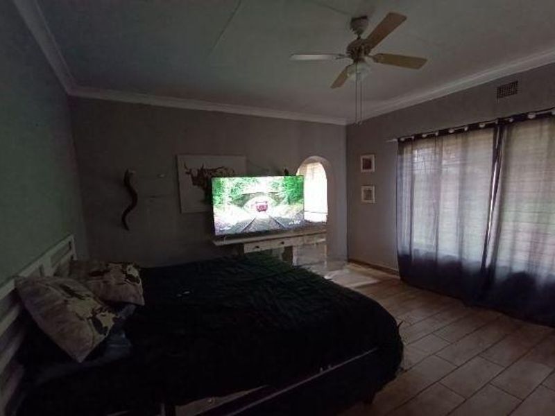 A bedroom featuring tiled flooring, a ceiling fan, and a decorative archway leading to an adjacent space.