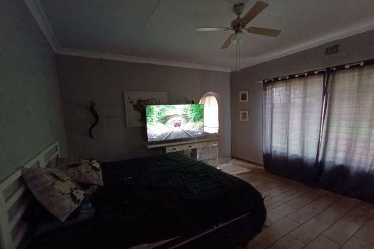 A bedroom featuring tiled flooring, a ceiling fan, and a decorative archway leading to an adjacent space.
