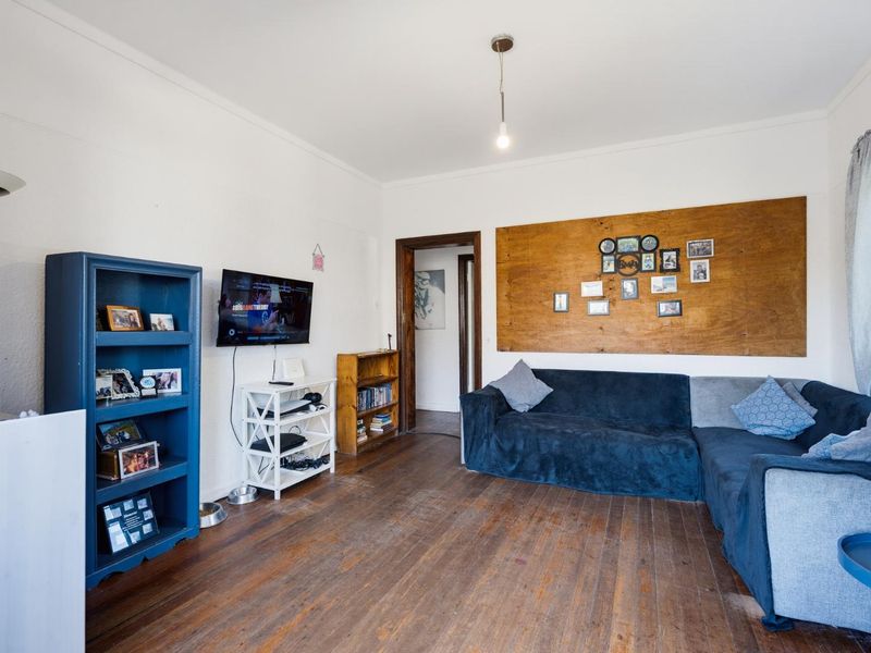 A living room featuring original hardwood flooring, coved ceilings, and a timber door frame, offering a blank canvas for renovation and modernization.