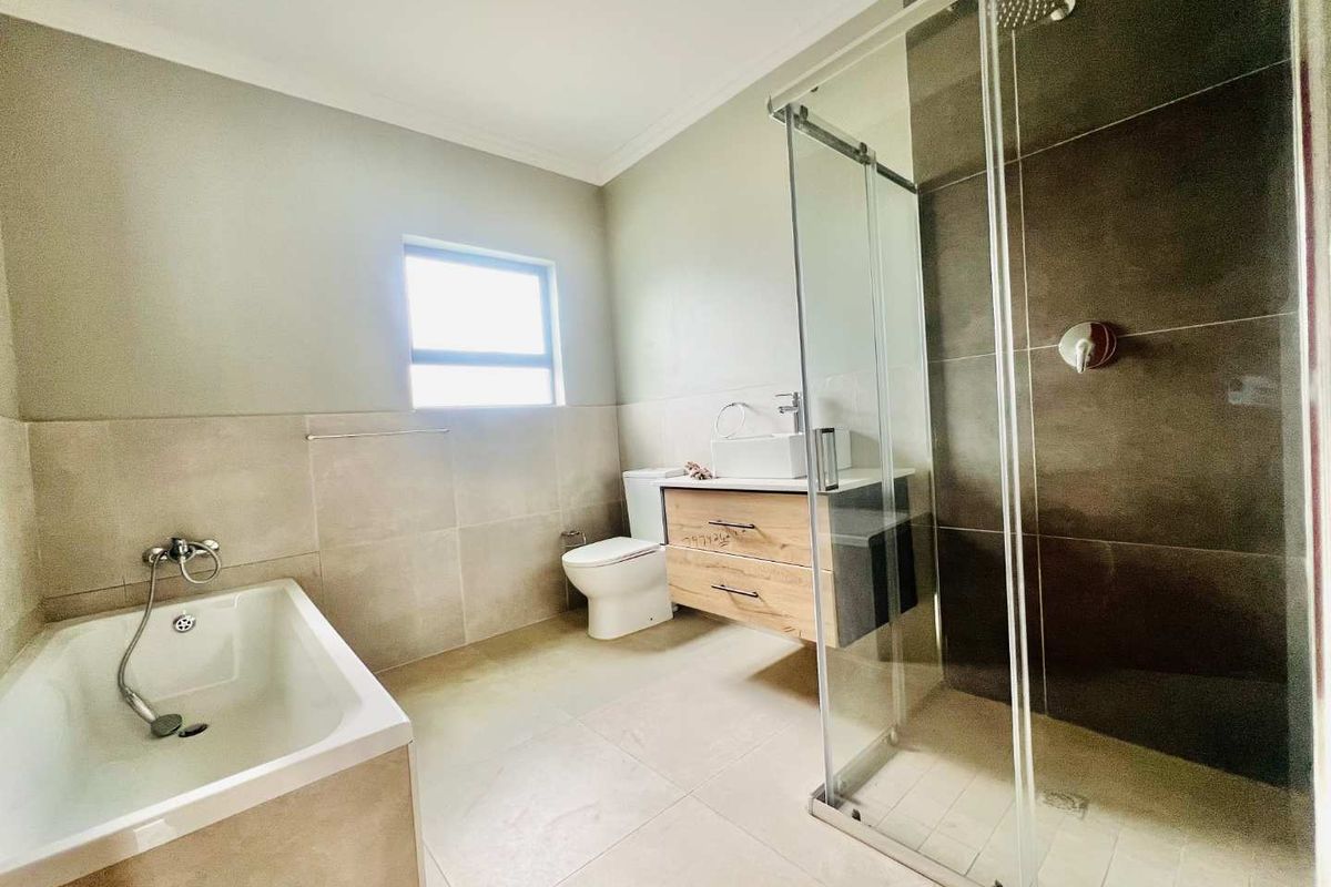 Modern bathroom featuring a floating vanity with vessel sink, a separate bathtub, and a spacious glass-enclosed shower with dark feature tiling.