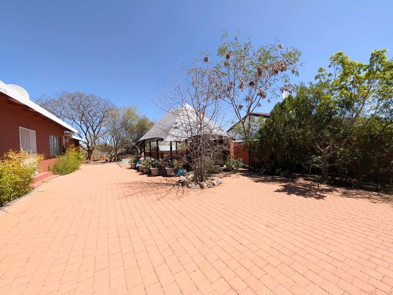 Spacious rear exterior area featuring extensive brick paving, a central thatched gazebo, and established garden surroundings.