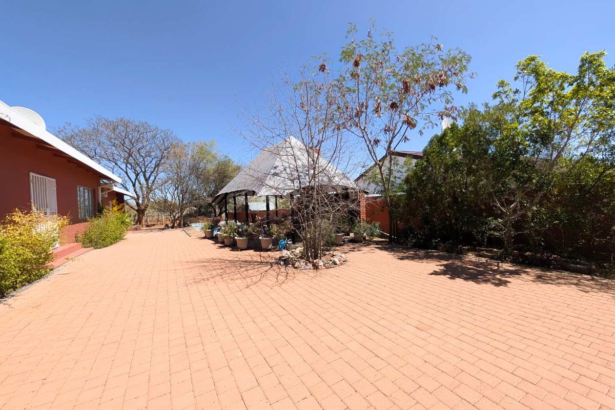 Spacious rear exterior area featuring extensive brick paving, a central thatched gazebo, and established garden surroundings.