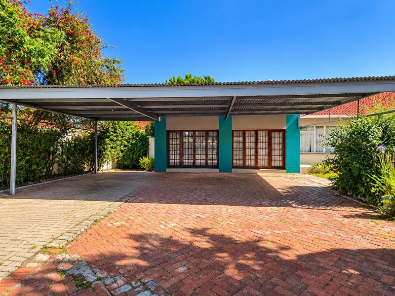 A spacious paved driveway featuring a large metal carport and direct access to the home through timber-framed glass doors.