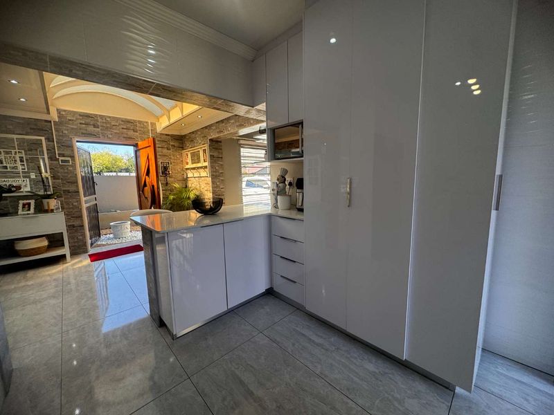 Modern open-plan kitchen area featuring high-gloss white cabinetry, stone countertops, and sleek tiled flooring, seamlessly connecting to an outdoor patio space.