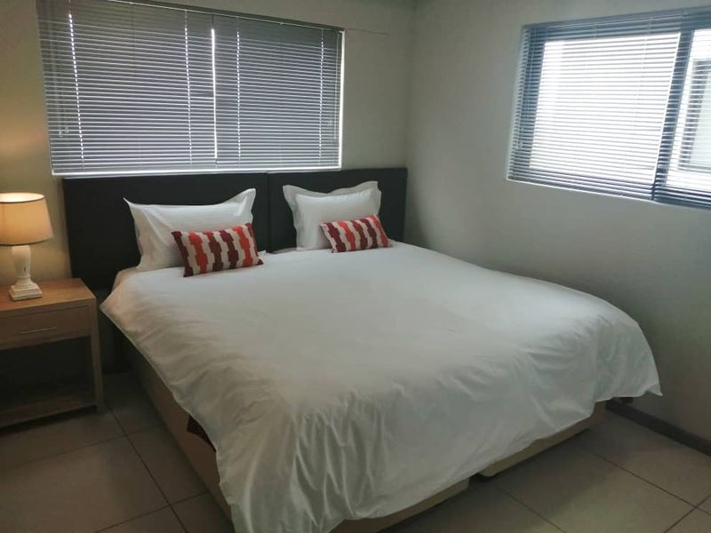 A bedroom featuring tiled flooring and dual windows fitted with venetian blinds.