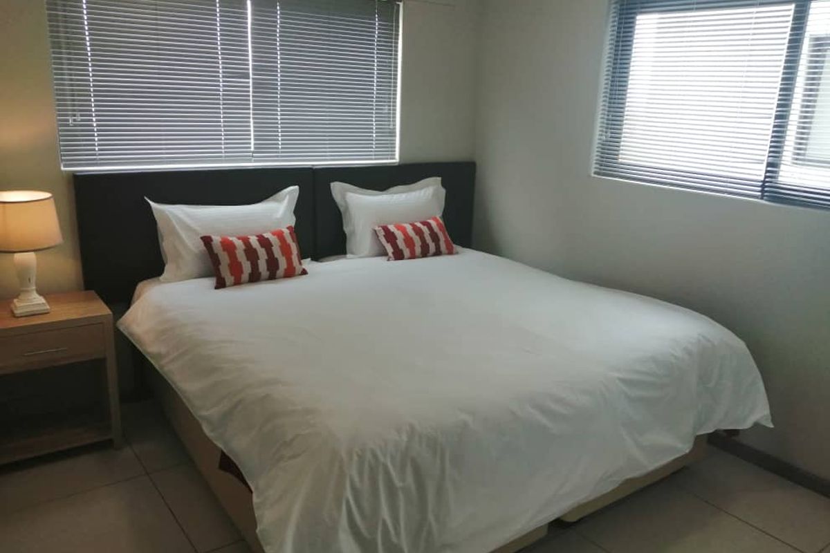 A bedroom featuring tiled flooring and dual windows fitted with venetian blinds.