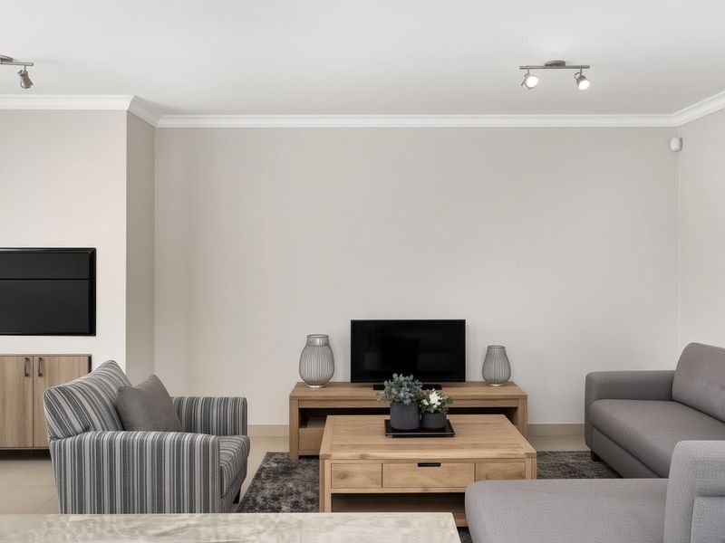 A well-maintained living room featuring neutral wall tones, ceiling coving, and modern track lighting, providing a clean and comfortable space.