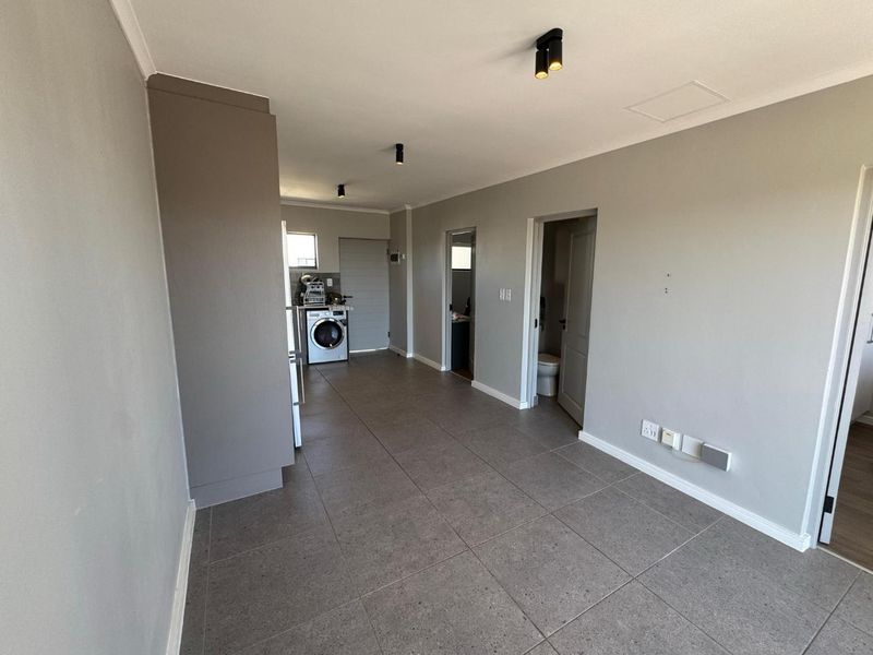 An open-plan living area featuring neutral grey walls, tiled flooring, and integrated laundry facilities, offering a clean and versatile space.