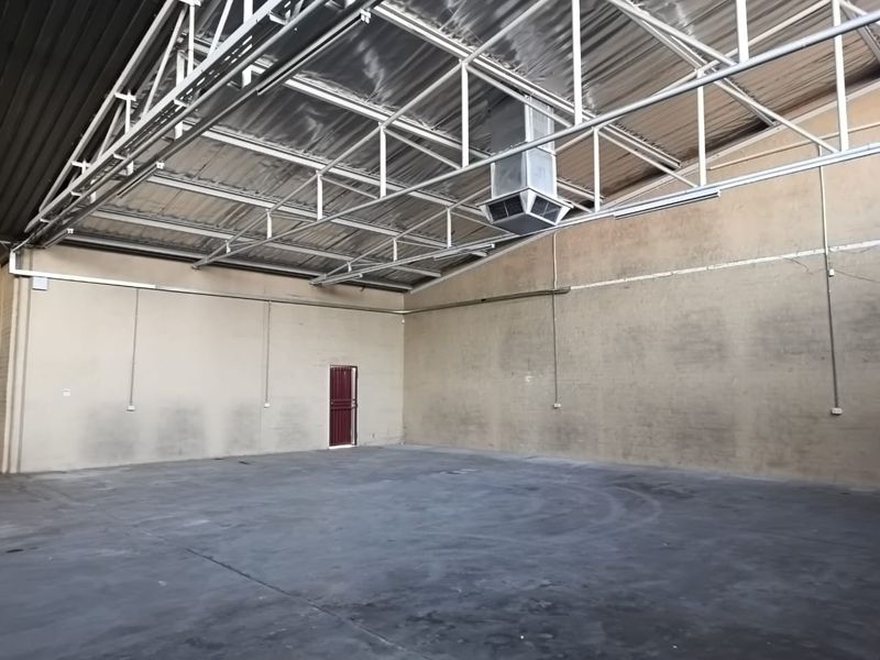 Spacious industrial office or warehouse area featuring exposed steel roof trusses, concrete flooring, and integrated HVAC ducting.