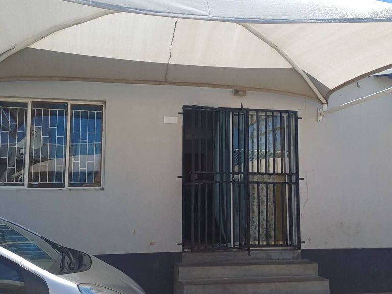 Front exterior view of the apartment featuring a protective shade sail, security gate, and burglar bars on the windows.