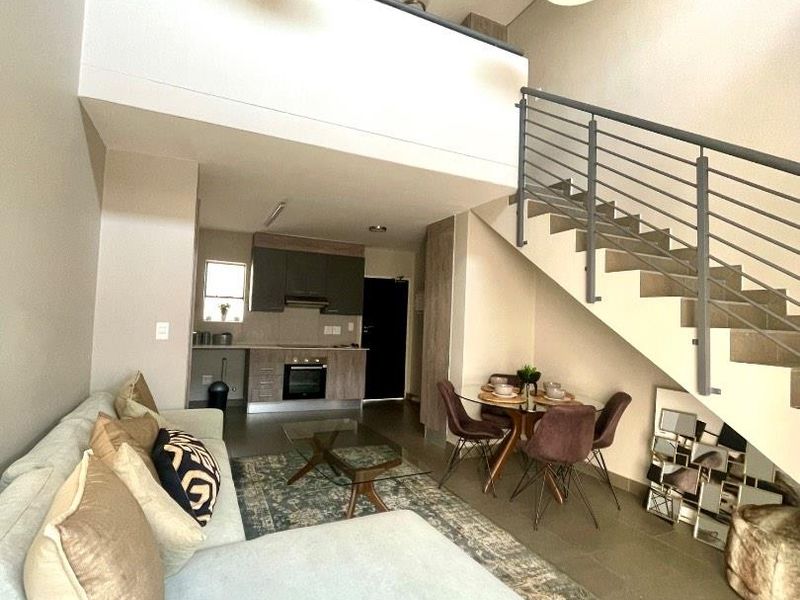 Open-plan living area featuring a modern kitchen, tiled floors, and a staircase leading to a mezzanine level with contemporary pendant lighting.