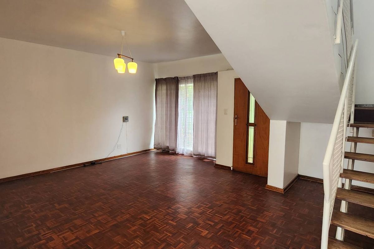 Spacious open-plan living area featuring original parquet flooring, a staircase with metal balustrade, and direct access to the exterior.