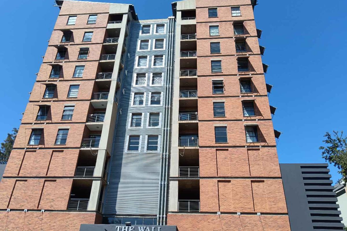 A modern multi-story apartment building featuring an exposed brick facade, integrated balconies with metal railings, and a central vertical architectural element.