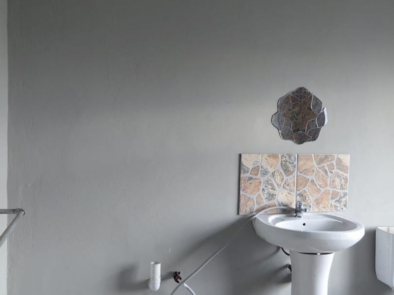 A basic bathroom featuring a pedestal basin with a tiled splashback and tiled flooring, currently requiring some finishing work on the plumbing connections.
