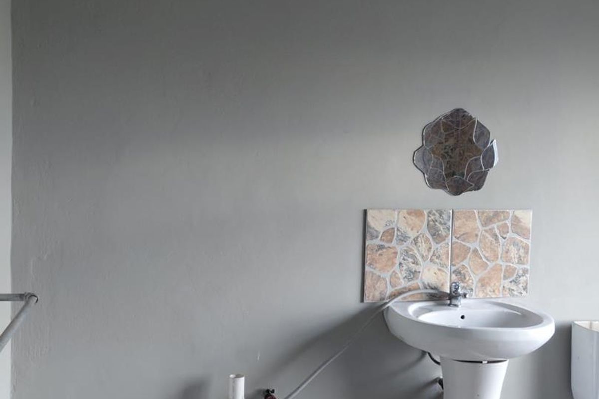 A basic bathroom featuring a pedestal basin with a tiled splashback and tiled flooring, currently requiring some finishing work on the plumbing connections.