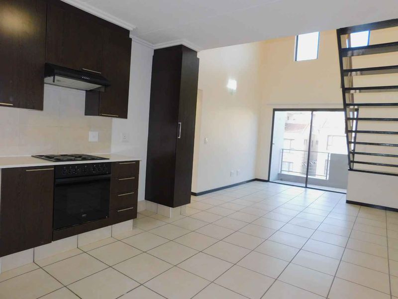 Open-plan living area featuring a modern kitchen with dark cabinetry, built-in appliances, tiled floors, and a staircase leading to an upper level.