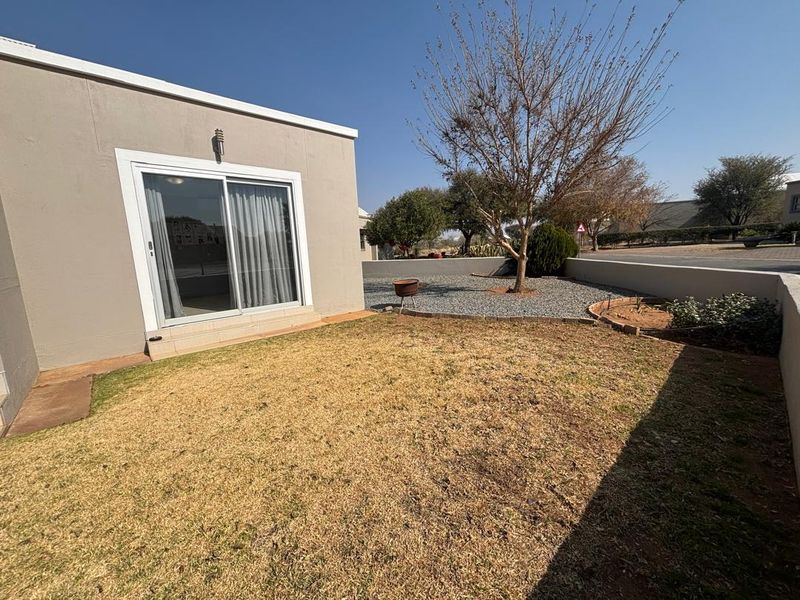 A rear exterior view of the property featuring a sliding glass door, a small lawn area, and gravel landscaping with a retaining wall.
