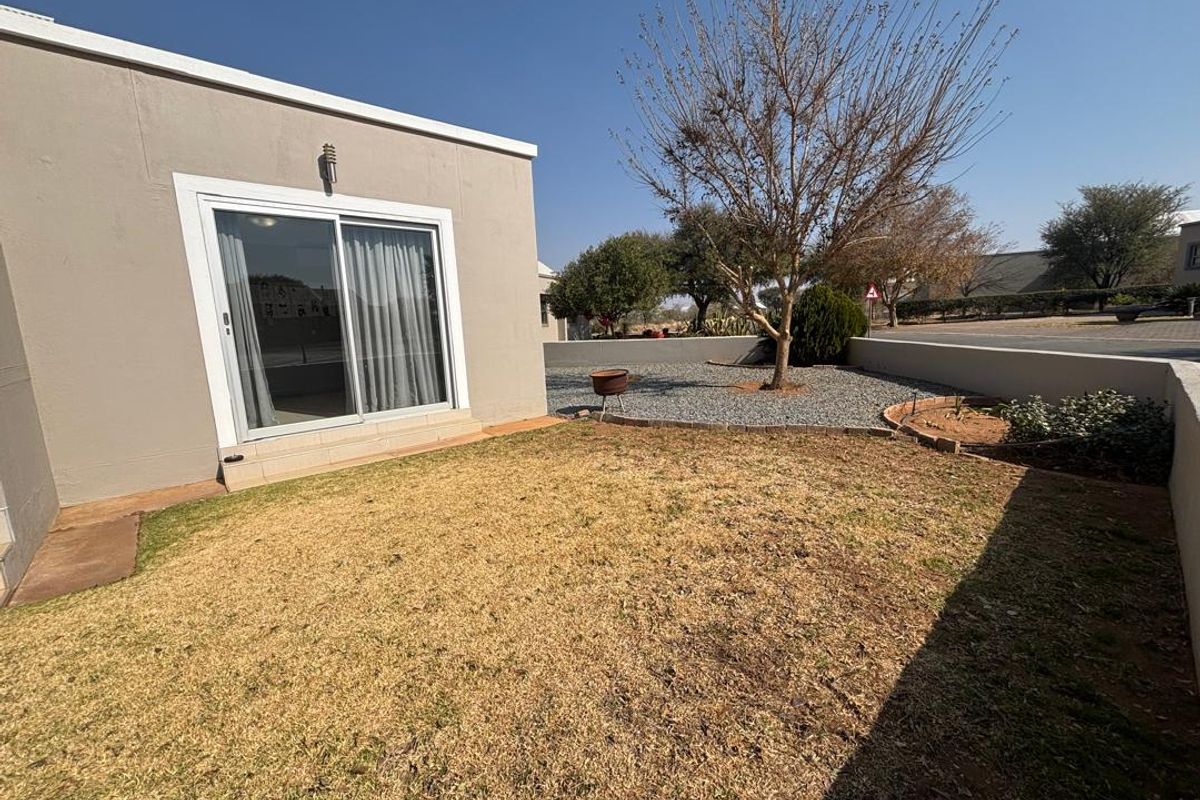 A rear exterior view of the property featuring a sliding glass door, a small lawn area, and gravel landscaping with a retaining wall.