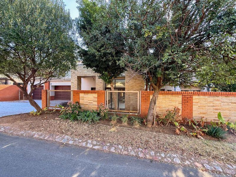 Front elevation of the property featuring a brick and stone boundary wall, gated entrance, and paved driveway leading to the garage.