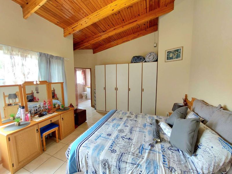 Spacious bedroom featuring a high vaulted timber ceiling, tiled flooring, and ample built-in wardrobe storage, with an adjoining en-suite bathroom.