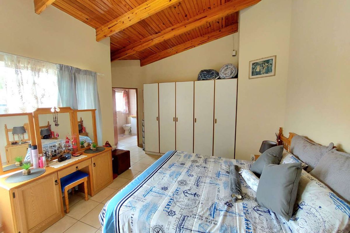 Spacious bedroom featuring a high vaulted timber ceiling, tiled flooring, and ample built-in wardrobe storage, with an adjoining en-suite bathroom.