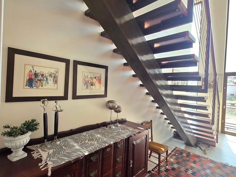 A bright hallway featuring a modern open-tread staircase with a metal balustrade and neutral tiled flooring.