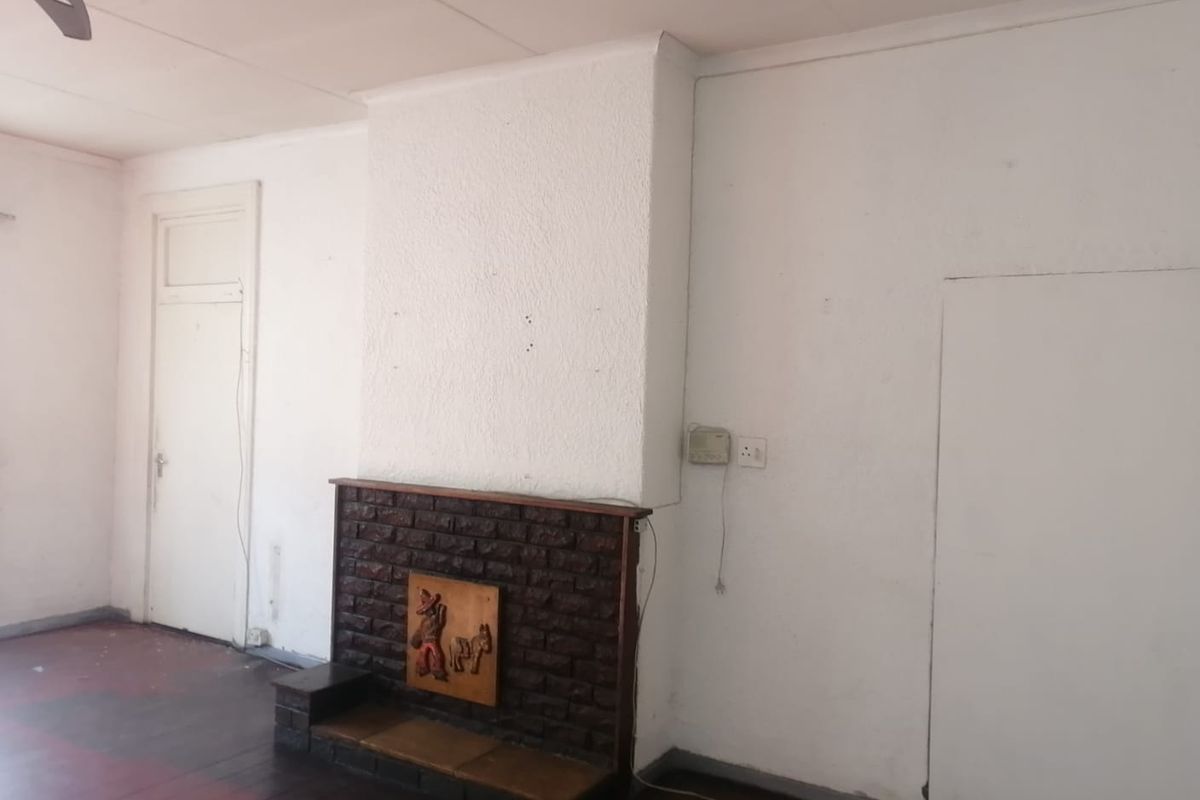 A living room featuring a traditional brick fireplace, wooden flooring, and a ceiling fan, offering a blank canvas for renovation.