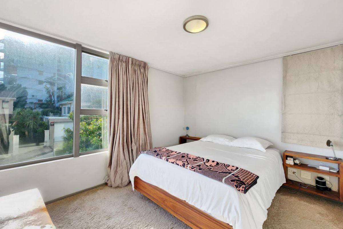 A bedroom featuring large windows, carpeted flooring, and a ceiling light fixture, offering a bright space with potential for modern updates.