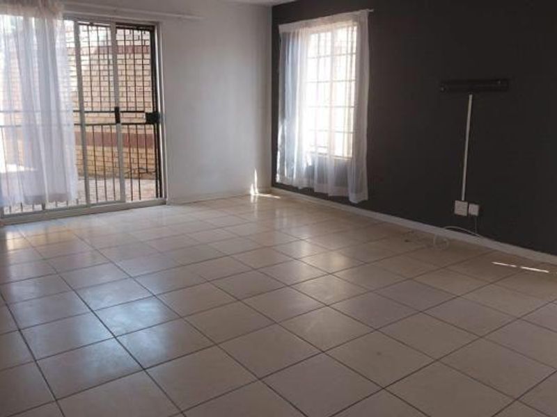 An empty, tiled living room featuring a sliding glass door with security gate and a dark accent wall.