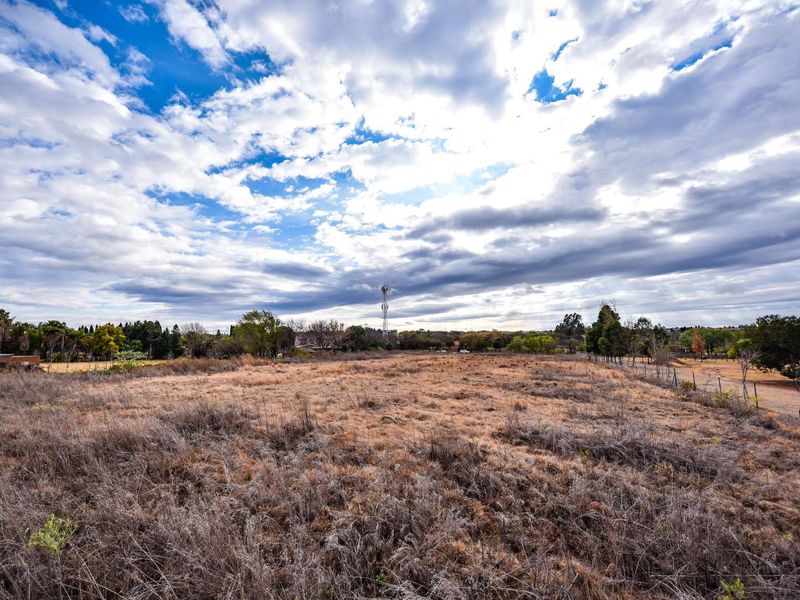A wide-angle view of a vacant residential plot featuring dry grass and perimeter fencing under a cloudy sky.