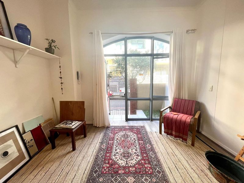 A bright living room featuring an arched window with garden access, neutral walls, and laminate flooring, offering a comfortable and well-lit living space.