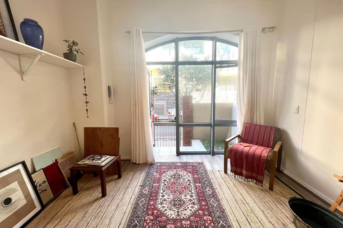 A bright living room featuring an arched window with garden access, neutral walls, and laminate flooring, offering a comfortable and well-lit living space.