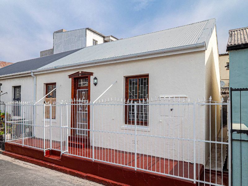Front facade of a cottage-style house featuring a corrugated metal roof, security gates, and a fenced front entrance area.