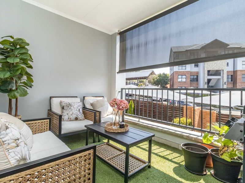 A well-maintained covered balcony featuring artificial grass flooring, a metal balustrade, and a retractable outdoor blind for privacy and shade.