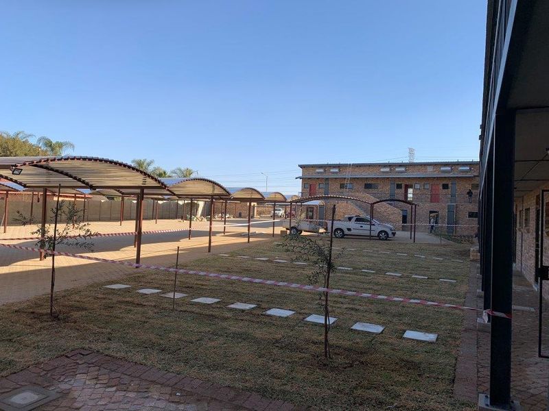 Exterior view of the apartment complex featuring a paved parking area with covered carports and a landscaped garden space.
