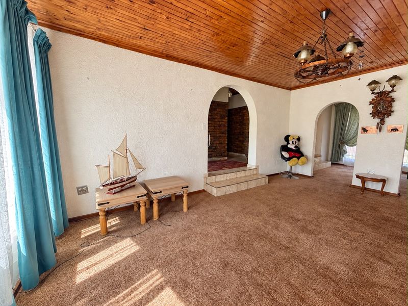 Spacious living area featuring a timber-clad ceiling, arched architectural transitions, and a raised tiled step leading to an adjacent room with exposed brickwork.