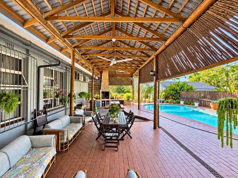 Spacious covered patio featuring a timber roof structure, built-in braai, and direct access to a swimming pool, perfect for outdoor entertaining.