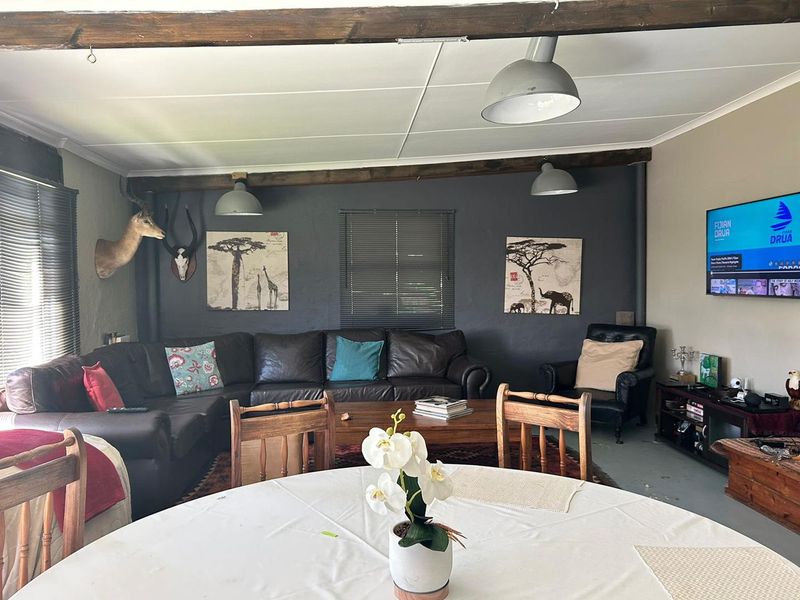 Open plan living and dining area featuring exposed timber ceiling beams, pendant lighting, and a dark feature wall.