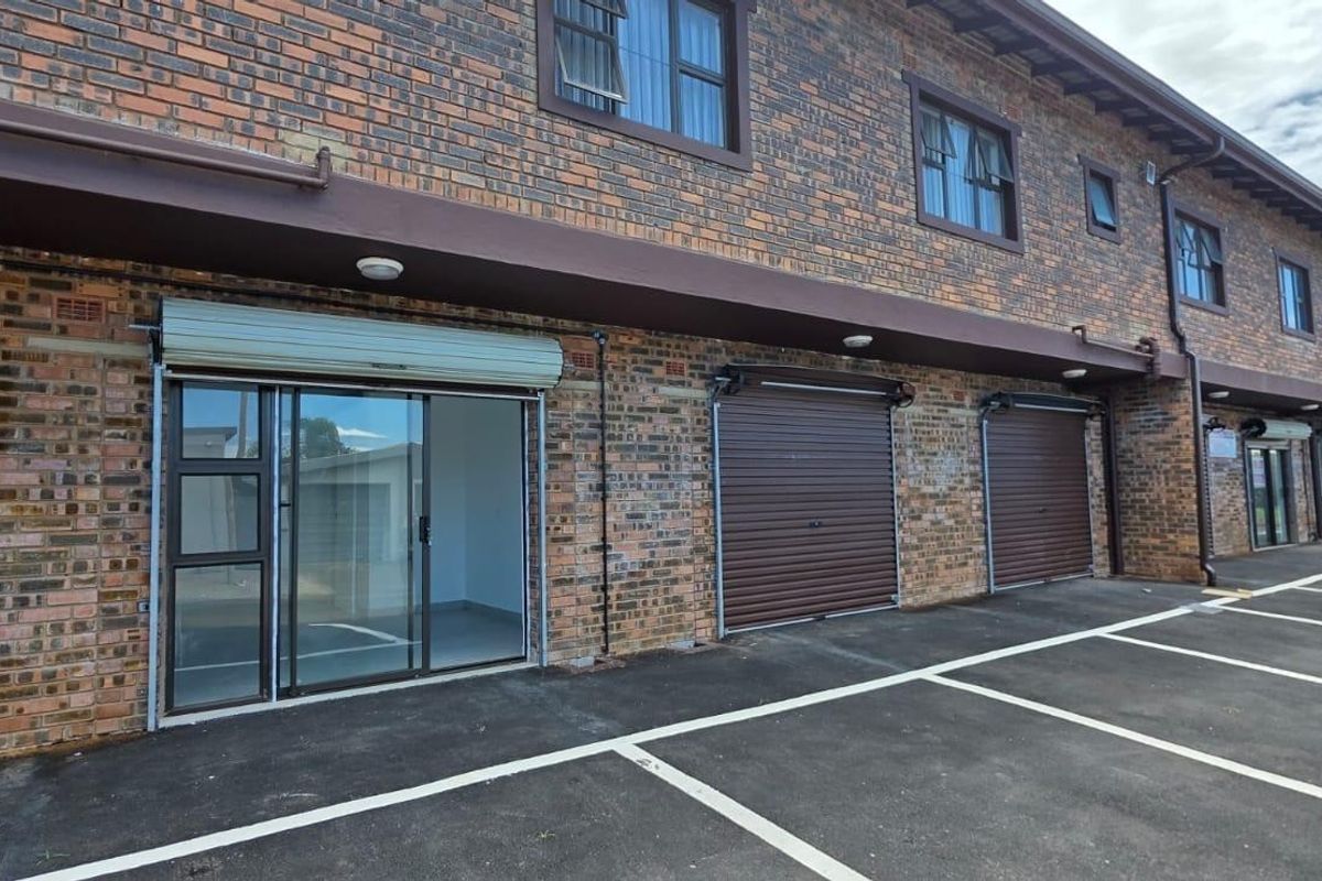 Front exterior view of a commercial retail property featuring face brick construction, roller shutter security doors, and dedicated asphalt parking bays.