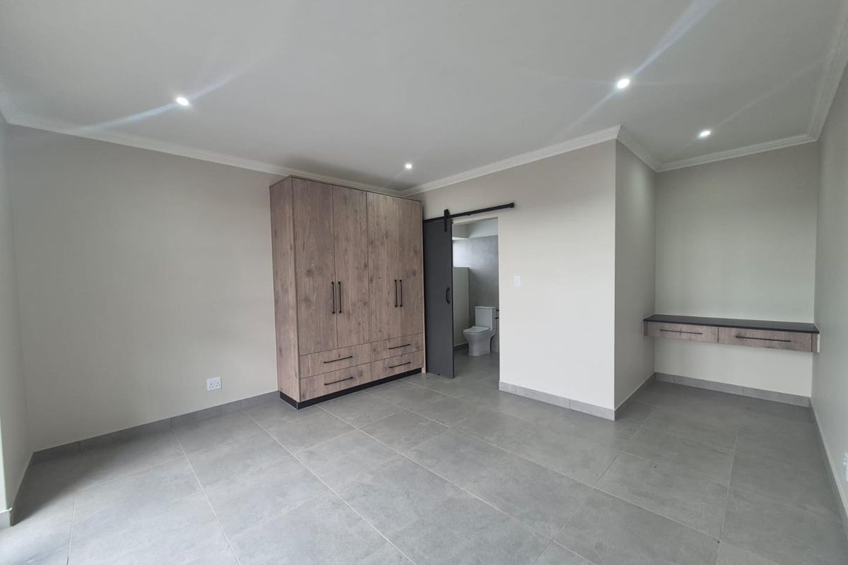 Spacious bedroom featuring modern grey floor tiles, built-in wooden cabinetry, a floating desk, and an en-suite bathroom accessed via a sliding barn door.
