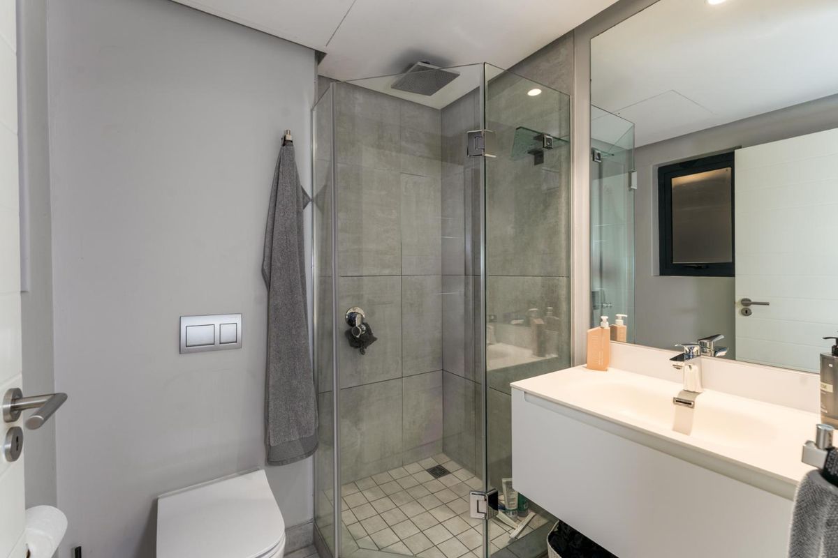 Modern bathroom featuring a glass-enclosed shower with rain head, wall-mounted toilet, and a sleek floating vanity with integrated basin.
