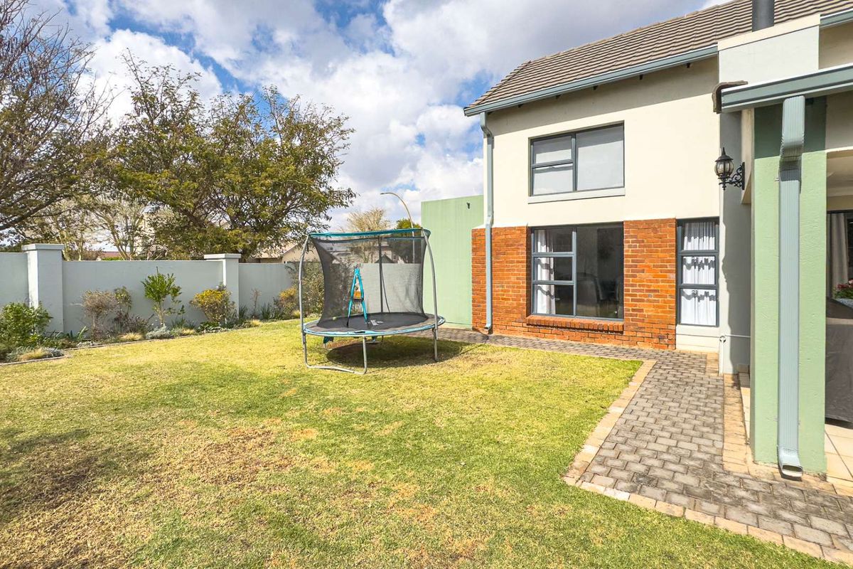 Rear view of the property featuring a landscaped garden, paved walkway, and a covered patio area.