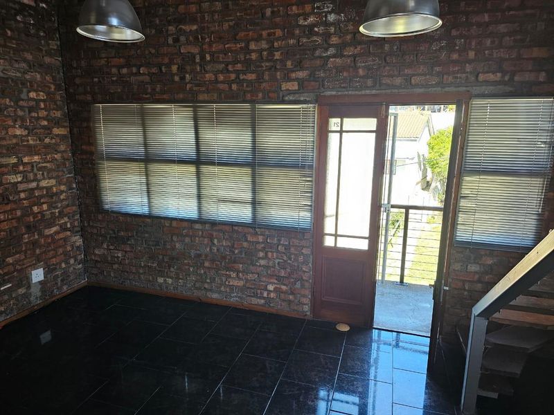 An empty living area featuring industrial-style exposed brick walls, dark tiled flooring, and direct access to an outdoor balcony space.